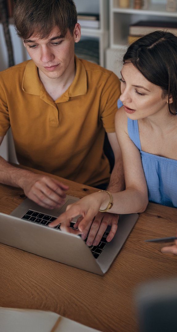 Zwei junge Erwachsene schauen interessiert auf einen Laptop. Symbolisiert Informationen von ENTEGA zu wichtigen Auswahlkriterien von Ökostromanbietern.