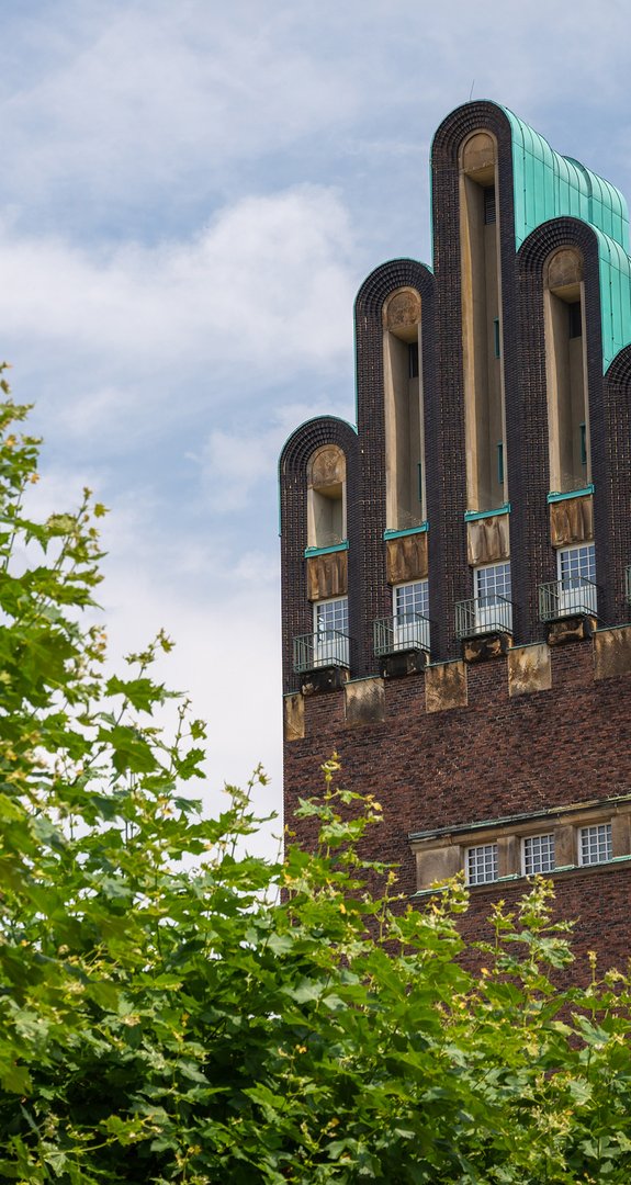 Hochzeitsturm in Darmstadt unter blauem Himmel, umgeben von Bäumen. Symbolisiert lokale klimafreundliche Gasversorgung.