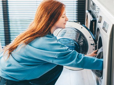 Frau befüllt Waschmaschine in moderner Küche; Thema: Stromverbrauch Waschmaschine und effiziente Nutzung im Alltag.