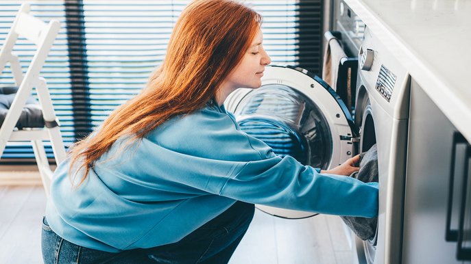 Frau befüllt Waschmaschine in moderner Küche; Thema: Stromverbrauch Waschmaschine und effiziente Nutzung im Alltag.