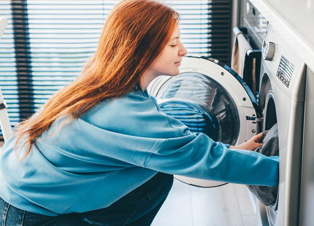 Frau befüllt Waschmaschine in moderner Küche; Thema: Stromverbrauch Waschmaschine und effiziente Nutzung im Alltag.