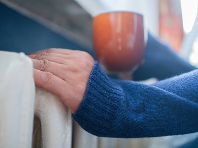 Bild zeigt Hände, die sich an einer Heizung wärmen. Es geht um das Berechnen des Gasverbrauchs von m³ in kWh.
