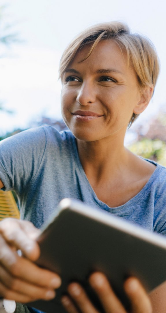 Lächelnde Person hält Tablet, umgeben von Natur. Sucht nach günstigen Tarifen.