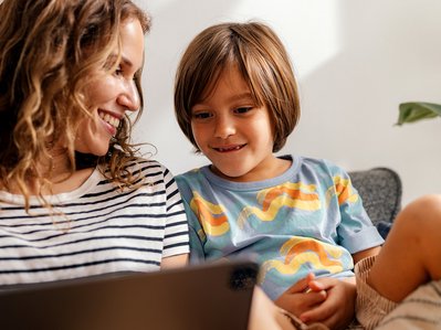 Frau und Kind sitzen auf Sofa, schauen gemeinsam auf Laptop; Stromanbieter wird recherchiert, entspannte Wohnumgebung.
