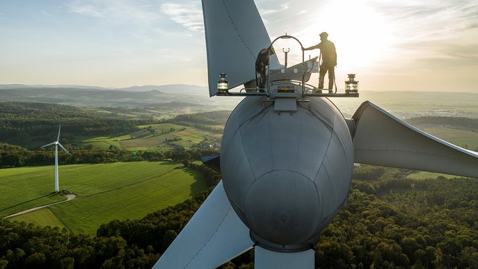 Techniker steht auf einem Windrad bei Sonnenuntergang, zeigt Engagement von ENTEGA für den Ausbau von 12 Windparks zur Ökostromerzeugung.
