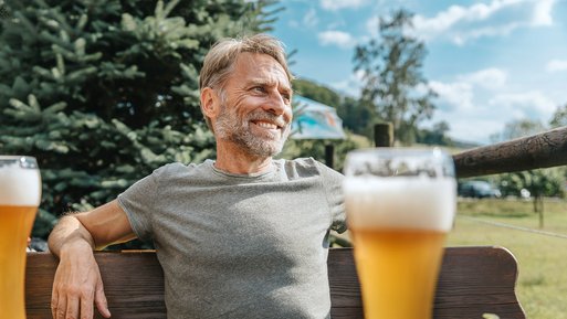 Mann sitzt entspannt auf Bank im Freien, genießt Weizenbier.