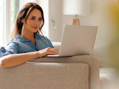 Frau sitzt entspannt auf einem Sofa im Wohnzimmer und arbeitet an einem Laptop. Symbolisiert Tipps von ENTEGA bei der Glasfaser-Einrichtung einer FRITZ!Box.