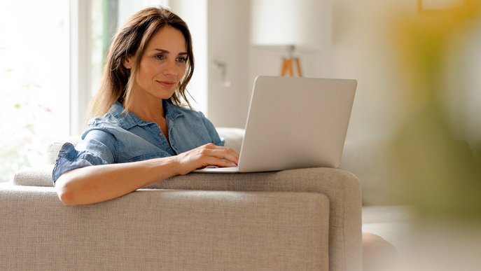 Frau sitzt entspannt auf einem Sofa im Wohnzimmer und arbeitet an einem Laptop. Symbolisiert Tipps von ENTEGA bei der Glasfaser-Einrichtung einer FRITZ!Box.