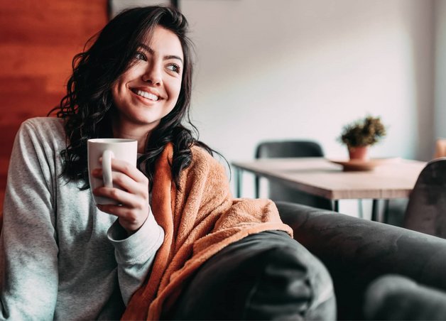 Bild zeigt eine lächelnde Frau mit Kaffeetasse – clevere Spartipps helfen ihr, Heizkosten zu senken.