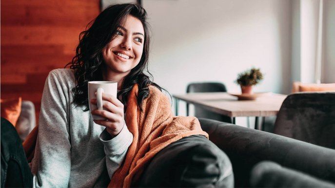 Bild zeigt eine lächelnde Frau mit Kaffeetasse – clevere Spartipps helfen ihr, Heizkosten zu senken.