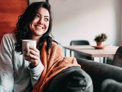 Bild zeigt eine lächelnde Frau mit Kaffeetasse – clevere Spartipps helfen ihr, Heizkosten zu senken.