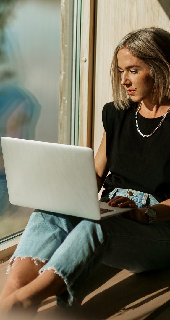 Frau sitzt an sonnigem Fenster mit Laptop, arbeitet konzentriert. Hohe Internetgeschwindigkeit durch Glasfaserausbau in Südhessen.