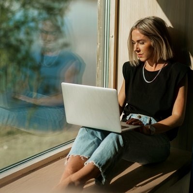 Frau sitzt an sonnigem Fenster mit Laptop, arbeitet konzentriert. Hohe Internetgeschwindigkeit durch Glasfaserausbau in Südhessen.
