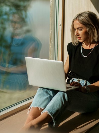 Frau sitzt an sonnigem Fenster mit Laptop, arbeitet konzentriert. Hohe Internetgeschwindigkeit durch Glasfaserausbau in Südhessen.