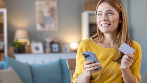 Frau im Wohnzimmer mit Smartphone, lächelt. App hilft kompatible Ladepunkte zu finden.