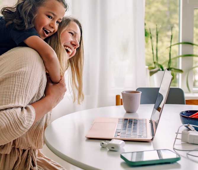 Lachende Mutter mit Kind auf dem Rücken vor Laptop. Symbolisiert sorgenfreies Zuhause mit ENTEGA-Paket für Strom, Internet und Telefon.