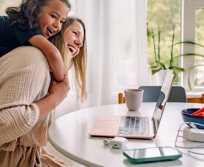 Lachende Mutter mit Kind auf dem Rücken vor Laptop. Symbolisiert sorgenfreies Zuhause mit ENTEGA-Paket für Strom, Internet und Telefon.