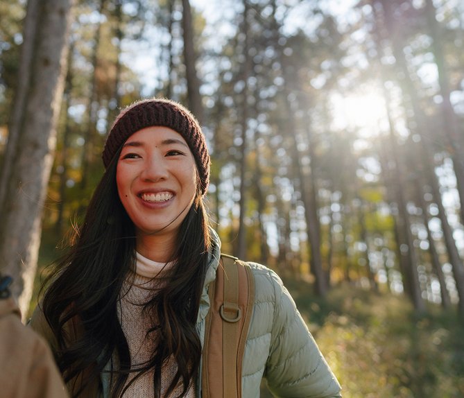 Zwei lächelnde Frauen im sonnigen Wald, symbolisieren zugänglichen Klimaschutz und Teilnahme an der Energiewende.