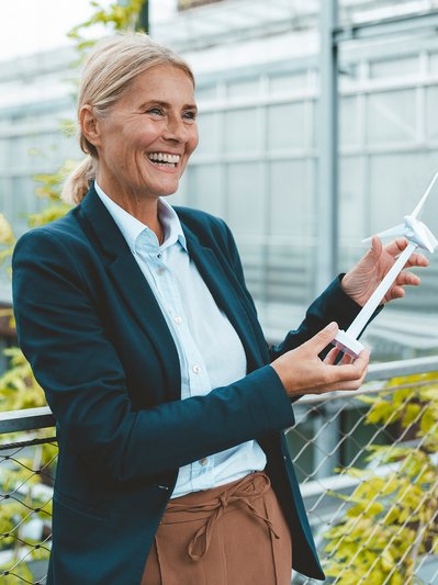Lächelnde Frau im Anzug hält ein Modell-Windrad, zeigt den Fokus auf erneuerbare Energien für ENTEGA Geschäftskunden.