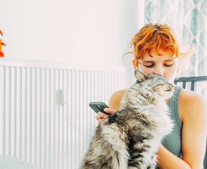Bild zeigt eine Frau, kuschelnd mit einer Katze vor einem Heizkörper, Symbolbild zum Thema „Gasheizung“