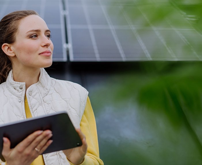 Frau mit Tablet vor Solarmodulen, entschlossenes Lächeln. Betonung auf kostengünstigen Solarstrom und 0 % Mehrwertsteuer-Vorteil.