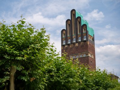 Hochzeitsturm in Darmstadt unter blauem Himmel, umgeben von Bäumen. Bekräftigt Darmstadts Engagement für umweltfreundliche Energie mit Fernwärme.