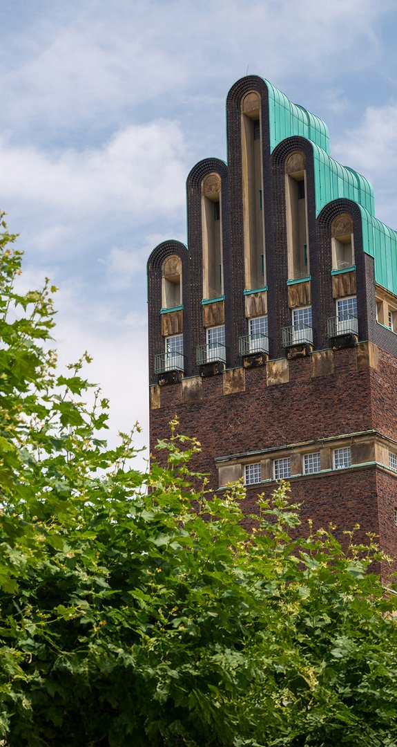 Hochzeitsturm in Darmstadt unter blauem Himmel, umgeben von Bäumen. Bekräftigt Darmstadts Engagement für umweltfreundliche Energie mit Fernwärme.