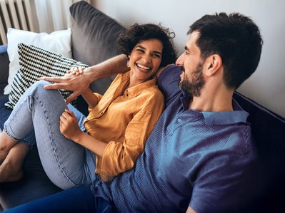 Lächelndes Paar entspannt auf einem Sofa. Ausdruck von Wohlbefinden durch Heizen mit 100 % Ökostrom.