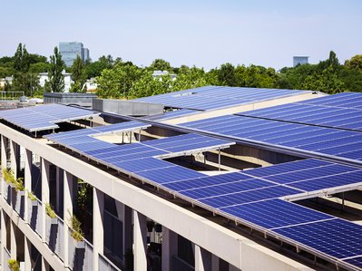  Große Solarmodule auf Dach eines Wohnkomplexes, umgeben von Bäumen, nutzen Sonnenenergie für umweltfreundlichen Mieterstrom.