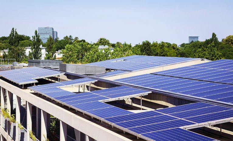  Große Solarmodule auf Dach eines Wohnkomplexes, umgeben von Bäumen, nutzen Sonnenenergie für umweltfreundlichen Mieterstrom.