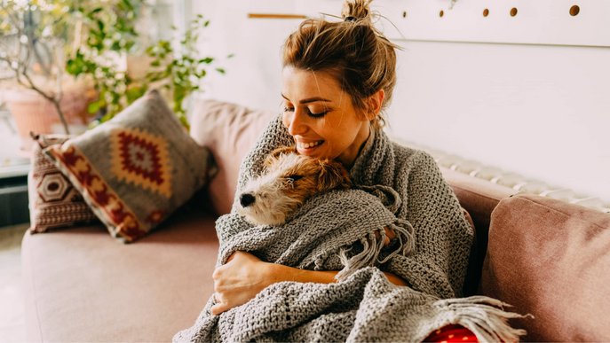 Bild zeigt lächelnde Frau mit Hund, eingekuschelt in eine Decke – Wissenswertes zum Thema Wärme.