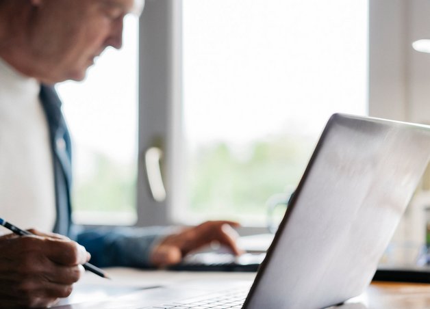 Person am Schreibtisch mit Laptop, Stift und Papier beim Jahresabrechnung selbst berechnen im Homeoffice.