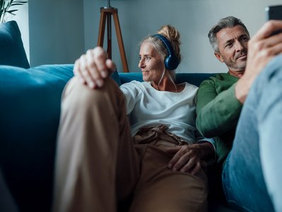 Entspanntes Paar auf Sofa, Frau mit Kopfhörern, Mann mit Smartphone. Symbolisiert schnelles Internet und Telefonie mit ENTEGA Home Kombi.