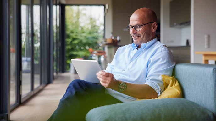 Älterer Mann analysiert Stromtarife auf Tablet, sitzt bequem zu Hause.