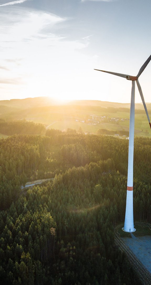 Windkraftanlagen in einer Waldlandschaft bei Sonnenaufgang. Symbol für erneuerbare Energie und Umweltschutz in harmonischer Naturkulisse.