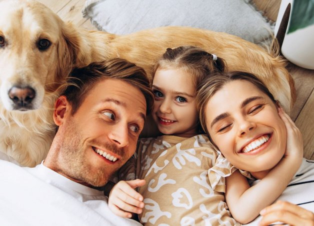 Eine Familie kuschelt mit ihrem Hund auf dem Wohnzimmerboden. Symbol für Alltag und den Stromverbrauch einer Familie.