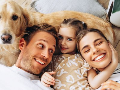 Eine Familie kuschelt mit ihrem Hund auf dem Wohnzimmerboden. Symbol für Alltag und den Stromverbrauch einer Familie.