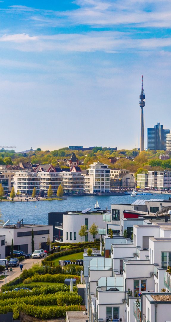 Weiße Neubauten am Ufer, Blick auf Dortmunds Zentrum mit Kirchtürmen und Fernsehturm, Symbol für Ökostrom Dortmund.