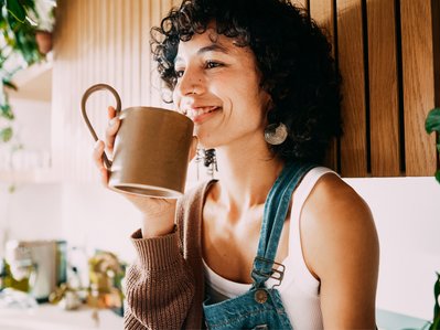 Lächelnde Frau mit einer Tasse in der Hand als Symbolbild für den Gasverbrauch von einer Person. 
