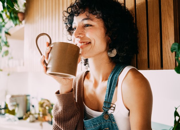 Lächelnde Frau mit einer Tasse in der Hand als Symbolbild für den Gasverbrauch von einer Person. 