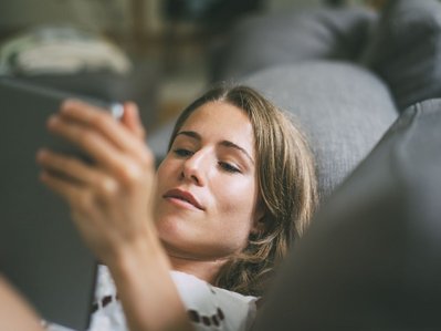 Eine Frau liegt mit einem Tablet auf dem Sofa und liest einen Ratgeber zu Stromversorger vs. Netzbetreiber.