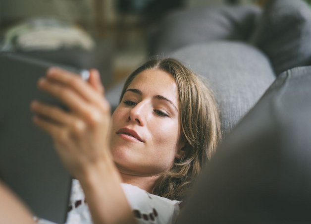 Eine Frau liegt mit einem Tablet auf dem Sofa und liest einen Ratgeber zu Stromversorger vs. Netzbetreiber.