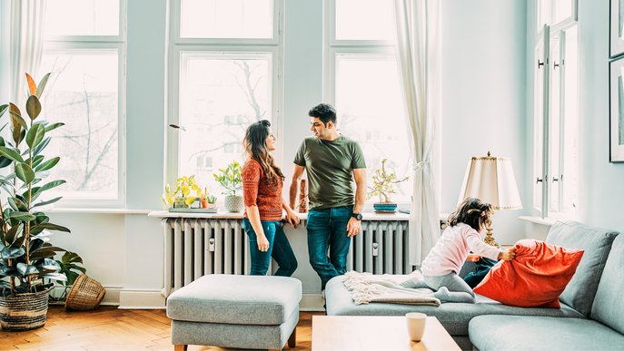 Bild zeigt eine dreiköpfige Familie im Wohnzimmer vor Heizkörpern als Stimmungsbild zum Thema nachhaltig heizen. 
