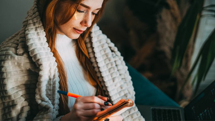 Stimmungsbild zeigt Frau beim Lesen eines Notizbuches, die Füße auf einem Heizkörper abgelegt