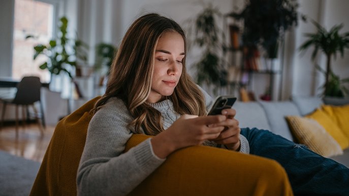Frau sitzt entspannt im Wohnzimmer und nutzt Smartphone. ENTEGA Cockpit App bietet volle Kostenkontrolle und Spartipps