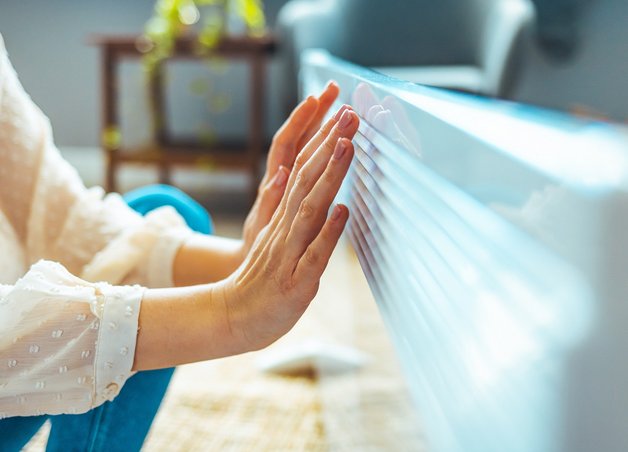 Bild zeigt eine Frau, die ihre Hände an einer Heizung wärmt – Elektroheizungen bieten vor allem in der Übergangszeit schnell verfügbare Wärme.