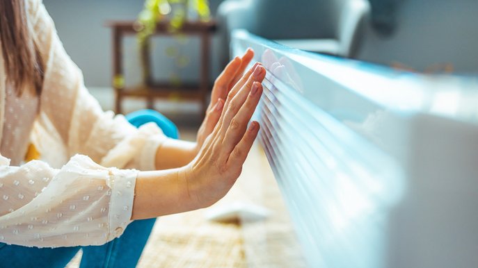 Bild zeigt eine Frau, die ihre Hände an einer Heizung wärmt – Elektroheizungen bieten vor allem in der Übergangszeit schnell verfügbare Wärme.
