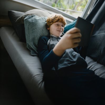 Junge entspannt sich auf dem Sofa mit Tablet in der Hand, zeigt Zufriedenheit. Verdeutlicht ENTEGA Zuhause Flat mit bequemem Ökostrom und Internet.