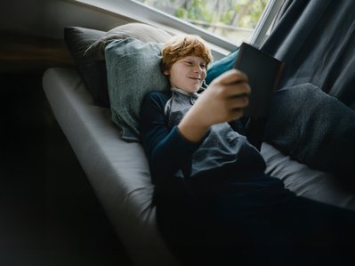 Junge entspannt sich auf dem Sofa mit Tablet in der Hand, zeigt Zufriedenheit. Verdeutlicht ENTEGA Zuhause Flat mit bequemem Ökostrom und Internet.