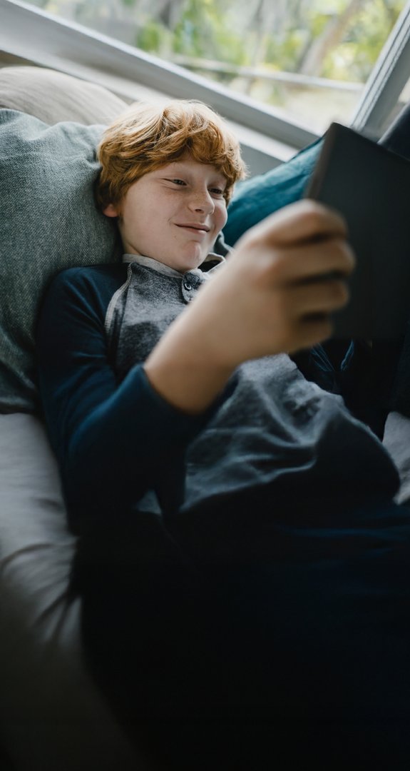 Junge entspannt sich auf dem Sofa mit Tablet in der Hand, zeigt Zufriedenheit. Verdeutlicht ENTEGA Zuhause Flat mit bequemem Ökostrom und Internet.